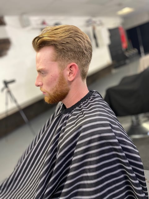 Man with blonde hair and beard in striped shirt, profile view in barbershop setting
