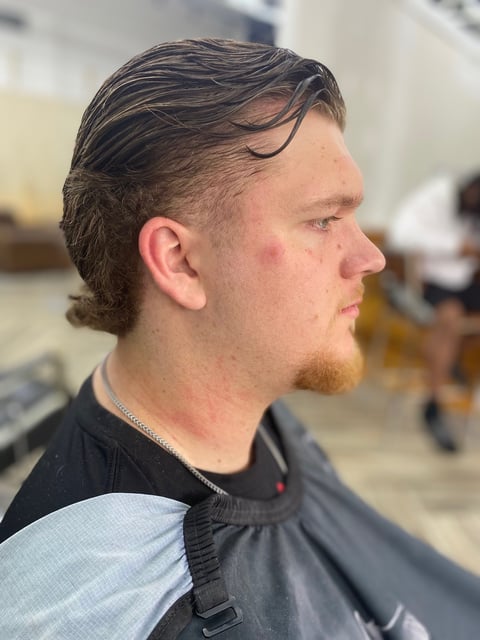 Side profile of a man with dark hair and a goatee wearing a black shirt, appearing to be in a barbershop or salon setting