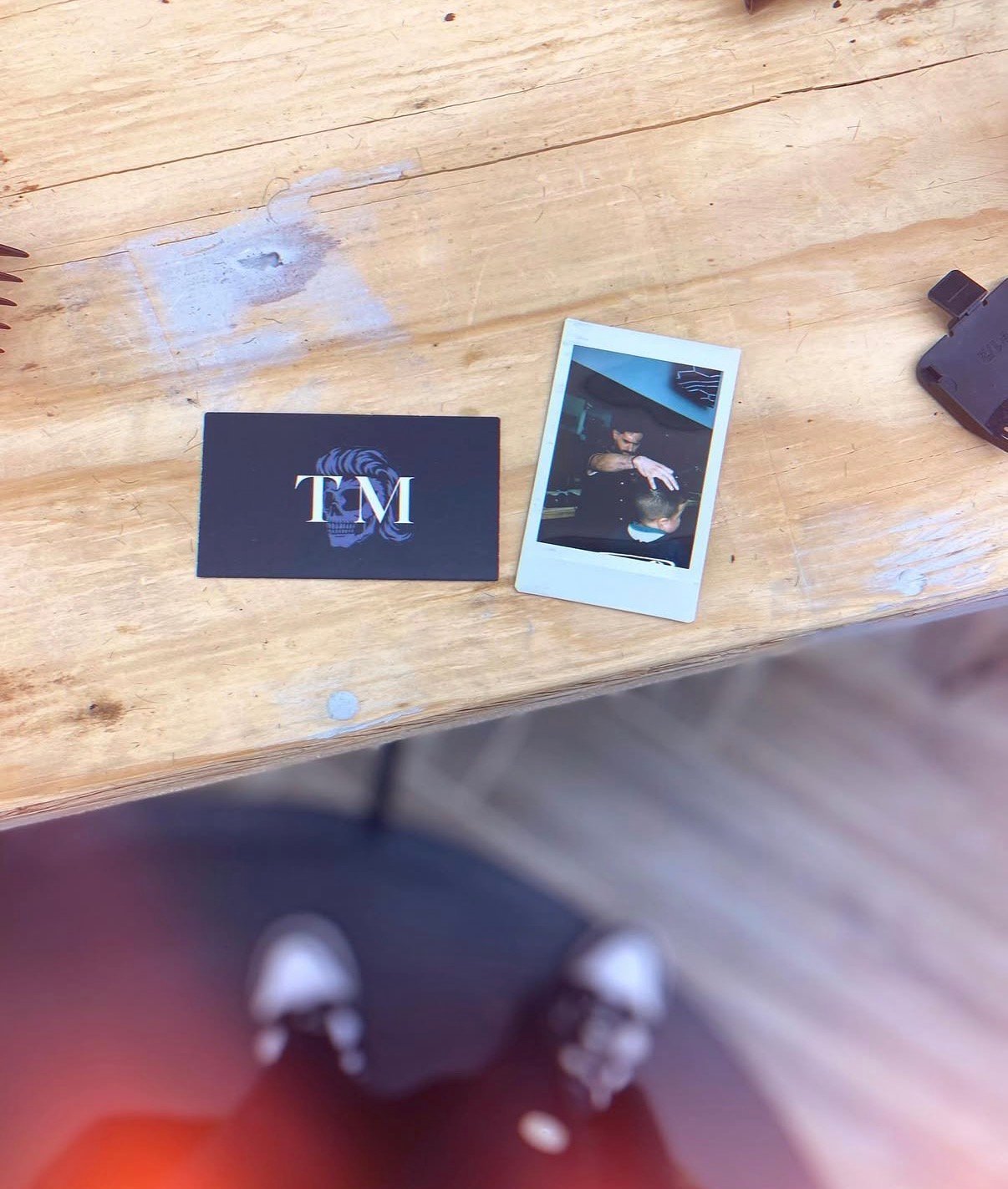 Navy business card with TM logo and instant photo on wooden table with blurred figures below