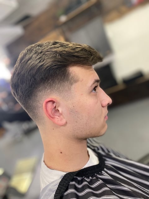 Man with short dark hair styled upward, faded sides, shown in profile view at a barbershop