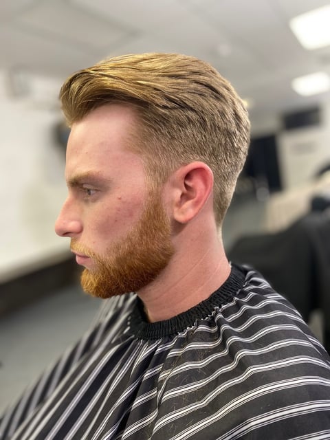 Man with blonde light brown hair and beard wearing black and white striped shirt in profile view inside an indoor space