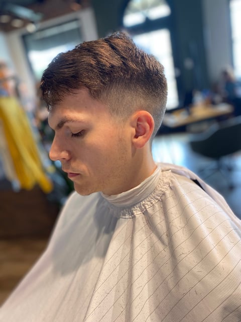Young man with a modern fade haircut and tapered sides in a barber shop setting